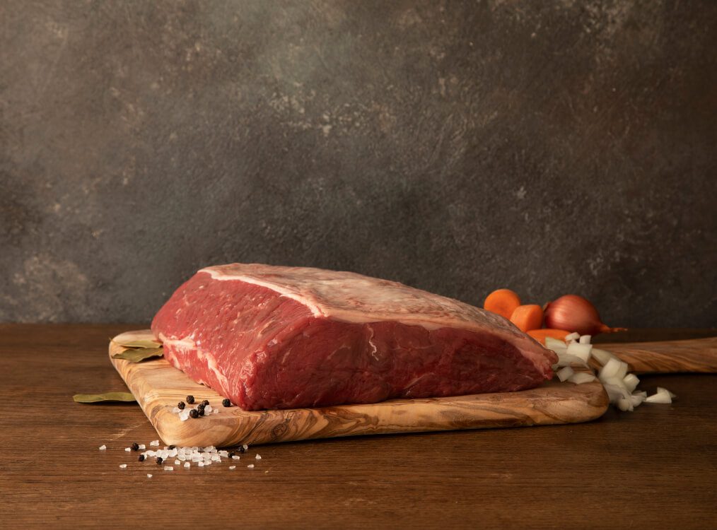 Beef Striploin on a wooden chopping board with mixed chopped vegetables