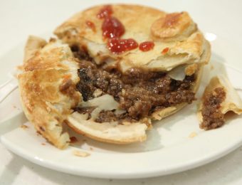 A mince beef and onion pie sitting on a white plate, with the contents of the pie visible.