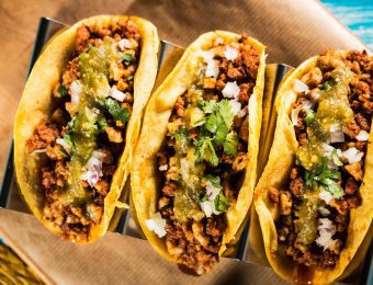 Three tacos with beef mince, chopped onion and salsa on top