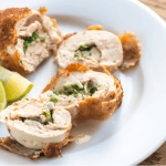 Chicken Kiev resting on a white plate, cut into slices. Some lemon wedges also sit on the plate. - Thumbnail Image