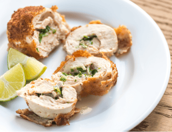 Chicken Kiev resting on a white plate, cut into slices. Some lemon wedges also sit on the plate.