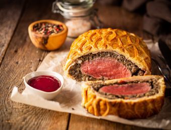 Beef Wellington sitting on some parchment paper, next to small dishes containing sauce and seasoning.