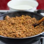 Mince is cooking in a black frying pan, which is sitting on a stove. Next to it is a white saucepan. - Thumbnail Image